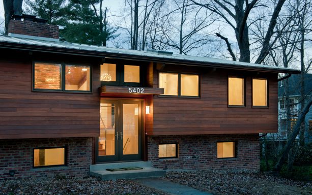 the remodeled house looks contemporary with new entry cover, black window and door frame, and horizontal wood wall cladding