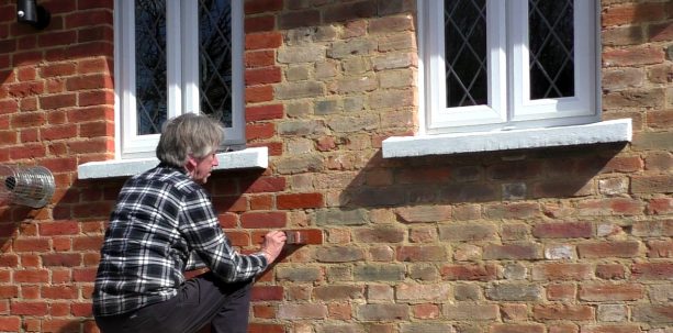 applying stain on old exterior brick wall by using brush