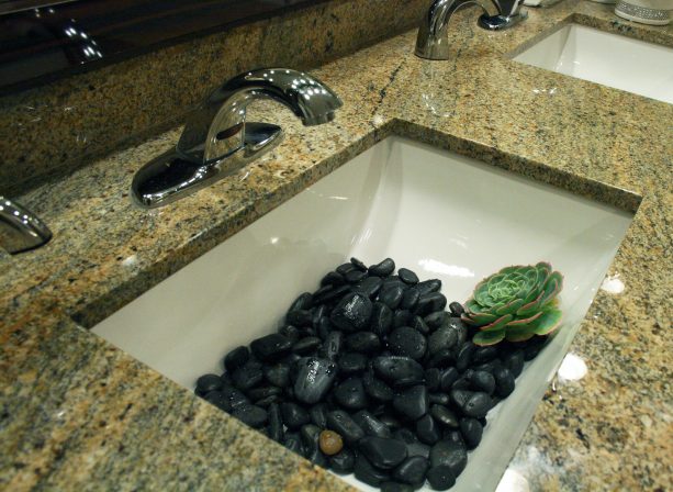 a modern white undermount sink with black river rocks decoration