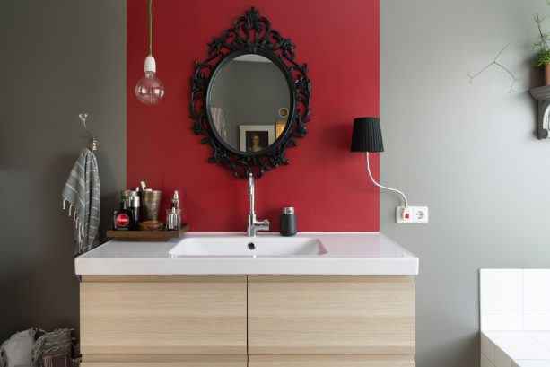 a red accent wall with black mirror in an eclectic bathroom