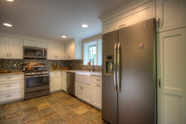 a slate refrigerator placed in a custom white recessed-panel cabinet
