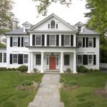 a white house with black shutters and coral red front door