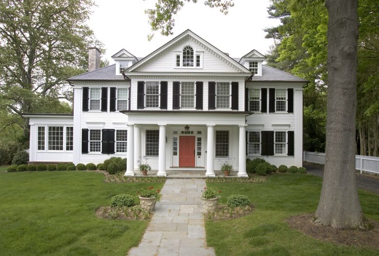 a white house with black shutters and coral red front door