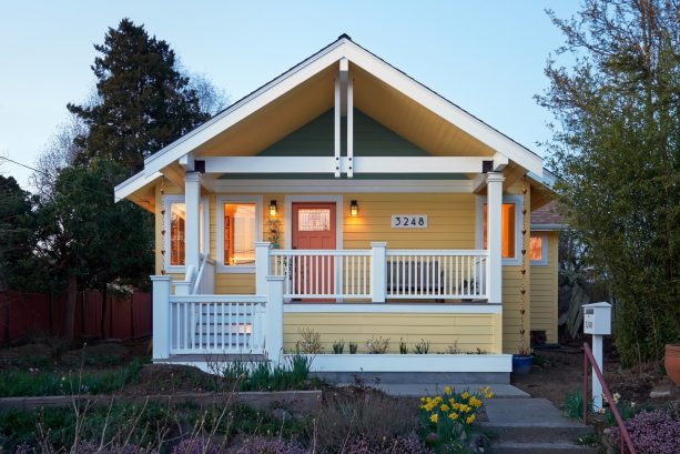 a soft yellow craftsman house with white trim, a bit of grey tone, and orange front door