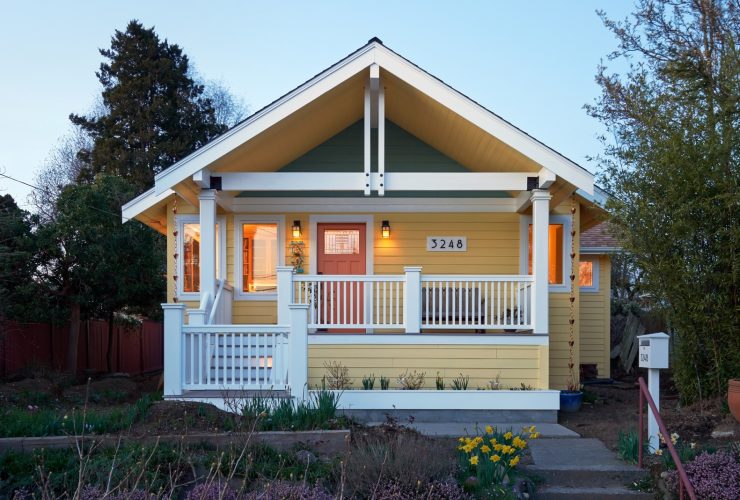 a soft yellow craftsman house with white trim, a bit of grey tone, and orange front door