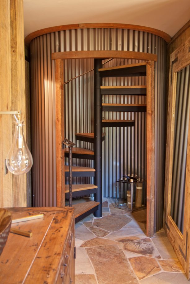 a spiral open staircase with corrugated metal surround in a rustic basement