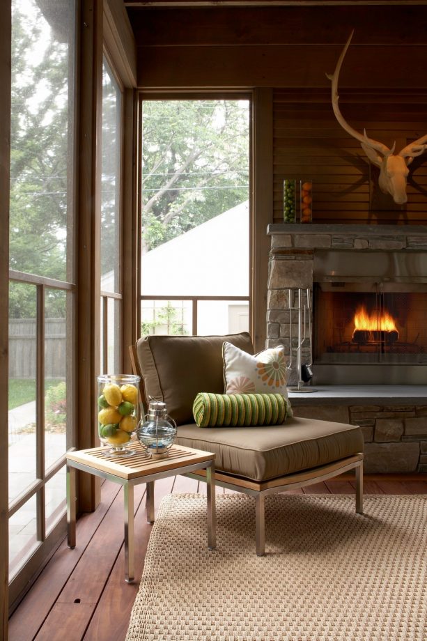 a screened porch with a reading spot near the fireplace