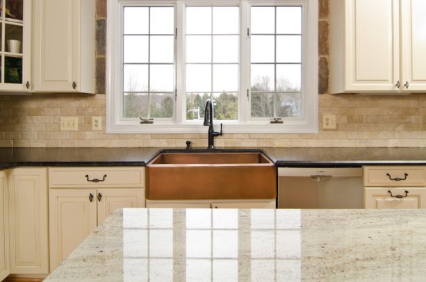 a copper farmhouse sink gorgeously paired with brown granite countertops and white cabinets