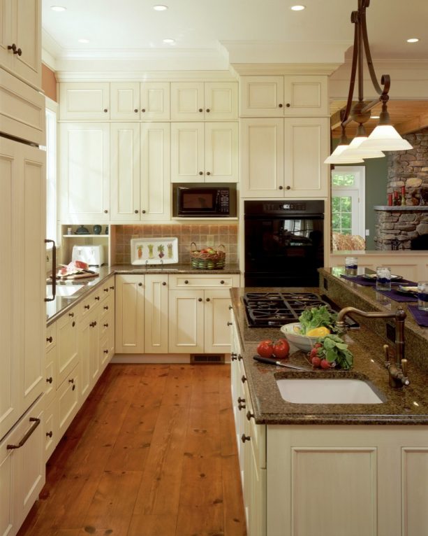 an elegant traditional kitchen design with creamy white cabinets, copper knobs, and brown granite for the countertops