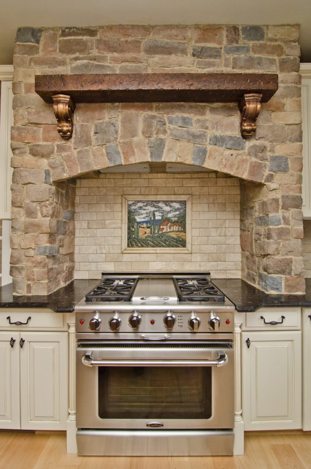 the stunning combination between white cabinets, brown granite countertops, and custom stone brick range hood