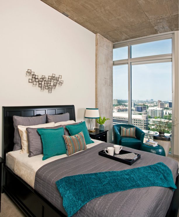 a black bed with grey bedding and teal pillows and throw blanket