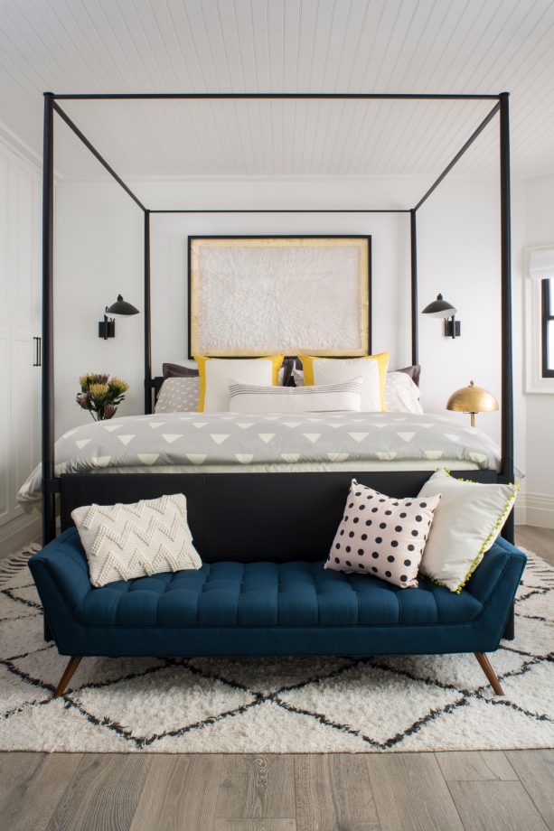 a black canopy bed paired with teal tufted bench at the end