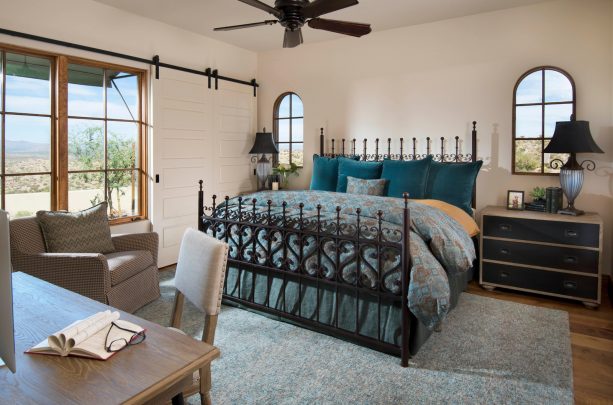 a black metal bed with gorgeous design and teal pillows in a Mediteranean-style bedroom