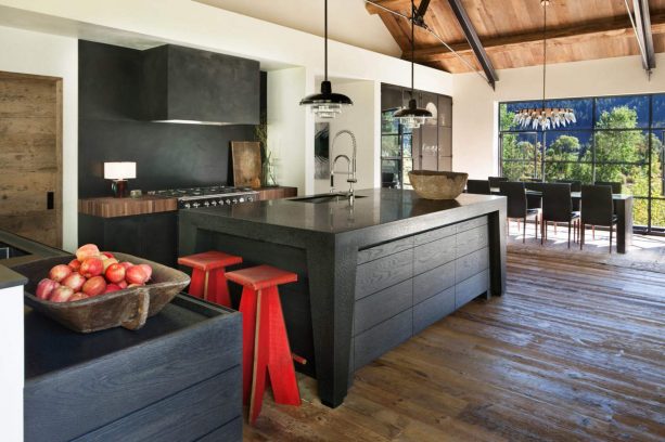 a rustic kitchen with black island, black cabinets, white walls, and red accentuating stools