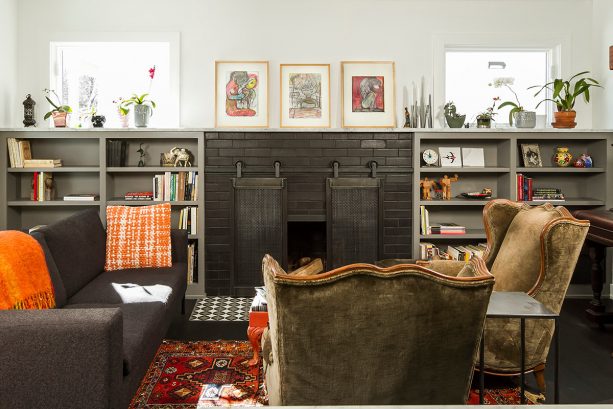 a black-painted brick fireplace with sliding, barn-style screen and a pair of grey bookshelves flanking it