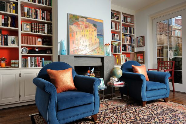 a simple black limestone fireplace paired with two built-in white bookshelves with orange back panels