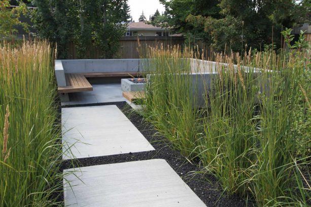 a contemporary landscape with crushed, black lava rocks, concrete pavers, and grassy plants