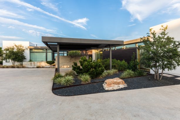 small black lava rock landscape with green plants near a modern carport area