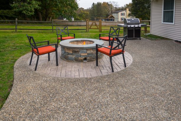 a backyard concrete patio with exposed aggregate and accentuating, round fire pit area