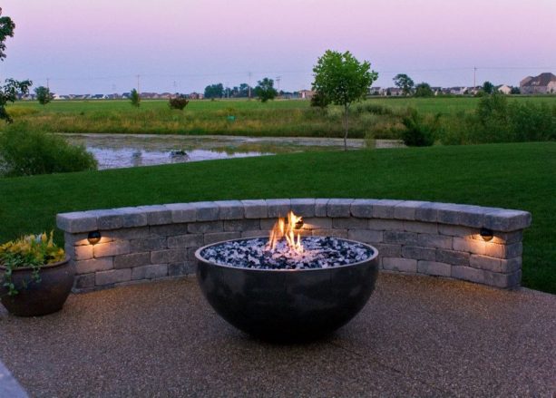a contemporary patio looks gorgeous with its stone seatwall, recessed lighting, a bowl-style fire pit, and an exposed aggregate concrete floor