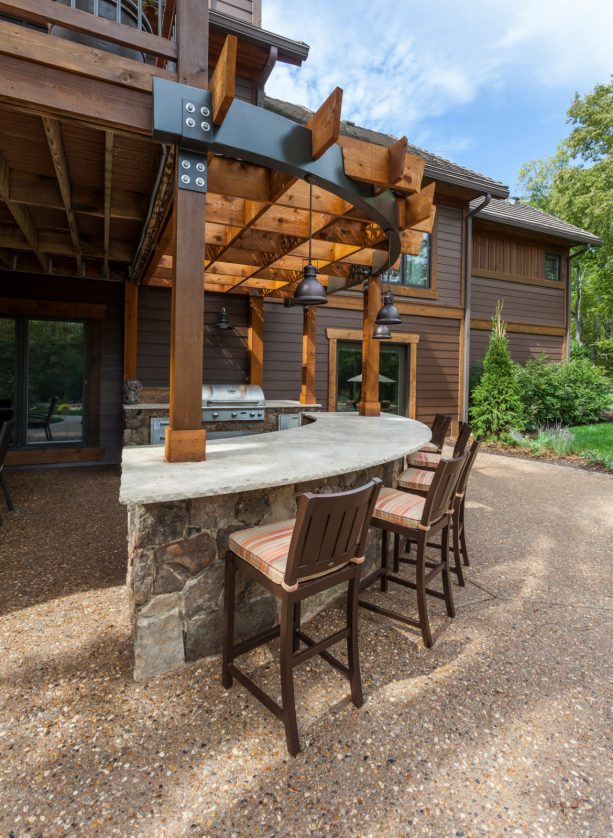 the earthy-tone exposed aggregate concrete floor of the patio complements the house and the outdoor kitchen design excellently