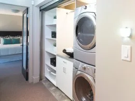 the laundry closet behind the roll up corrugated metal door is completed with cabinets and stacked washer and dryer
