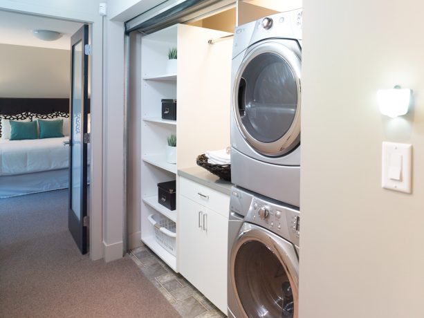 the laundry closet behind the roll up corrugated metal door is completed with cabinets and stacked washer and dryer