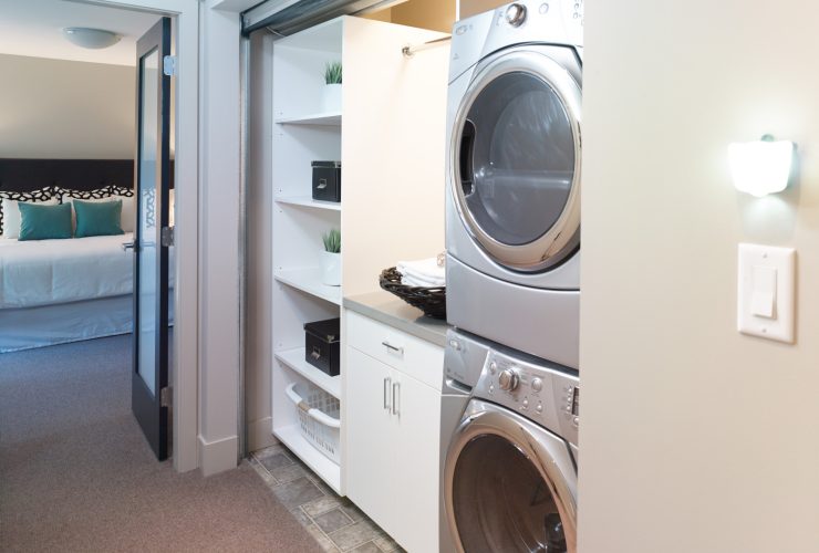the laundry closet behind the roll up corrugated metal door is completed with cabinets and stacked washer and dryer