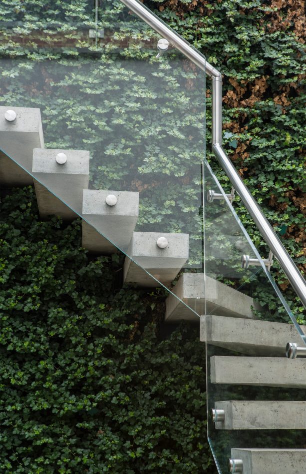a contemporary concrete stair design with glass railing and metal, round tube handrail